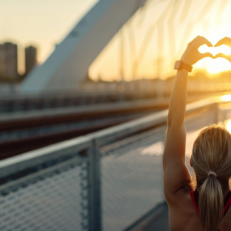 Rear view of athletic woman showing heart shape at sunset.