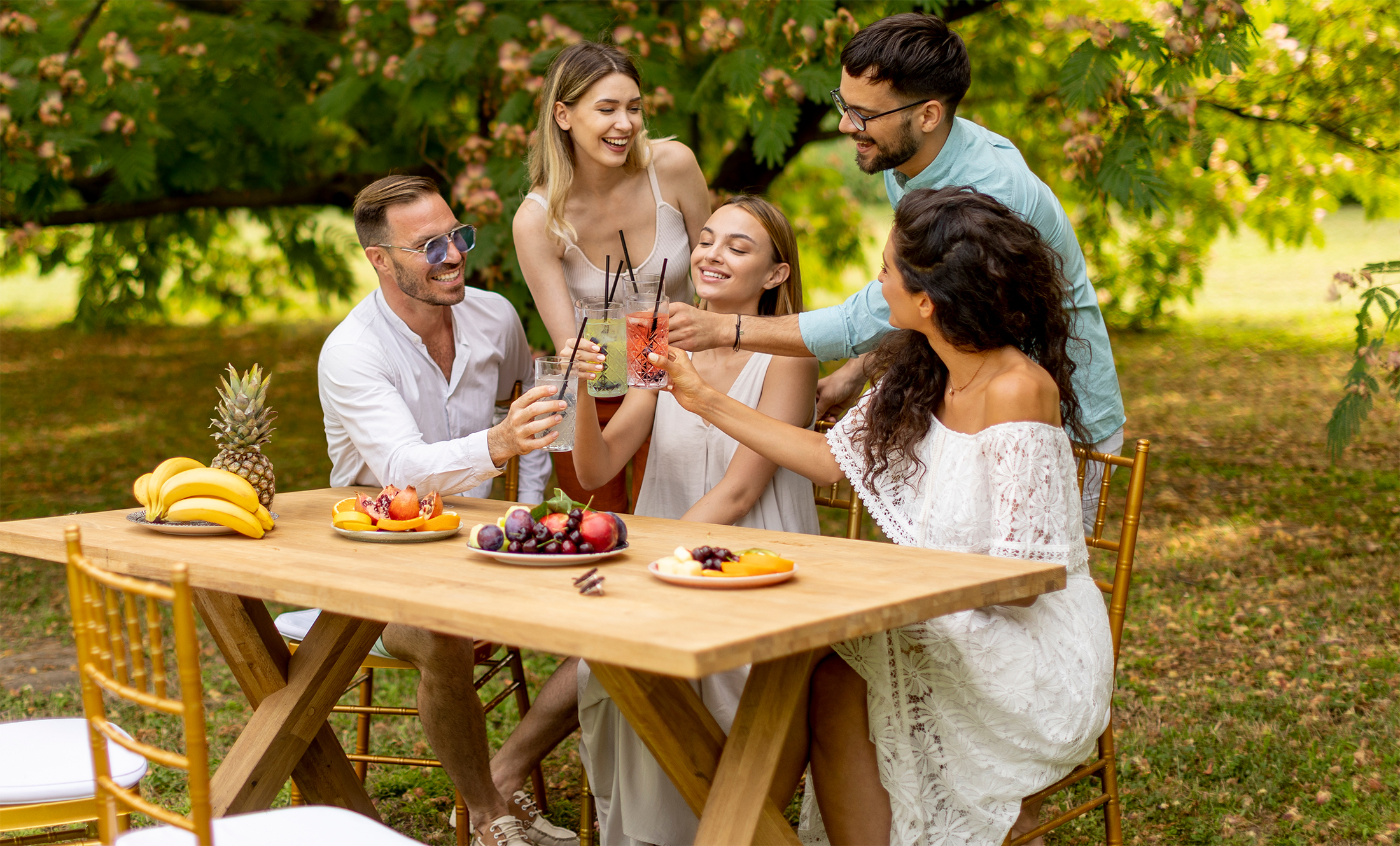 group-happy-young-people-cheering-with-fresh-lemonade-eating-fruits-garden